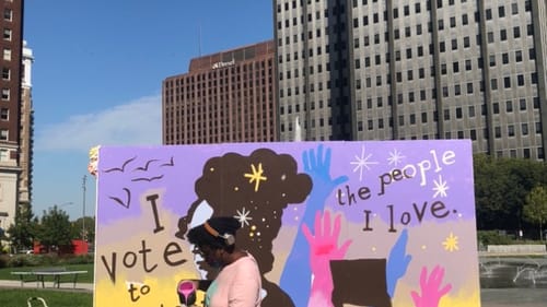 Artist Kah Yangni works on a mural that reminds us our vote is a way to show our love. (Photo by Alaina Johns.)