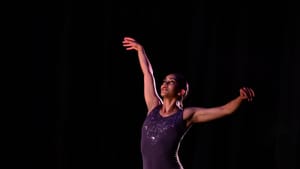 Pérez-Vega, a Puerto Rican woman dancing solo in a purple leotard, poses gracefully mid-stride with her arms lifted.