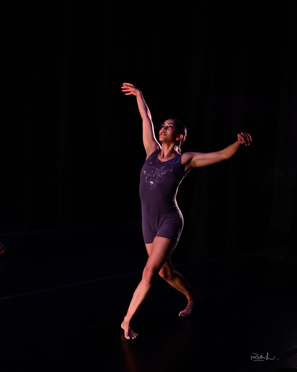 Pérez-Vega, a Puerto Rican woman dancing solo in a purple leotard, poses gracefully mid-stride with her arms lifted.