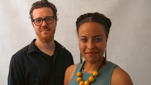 Keisha and Doug pose for a portrait style photo against a cream/beige backdrop