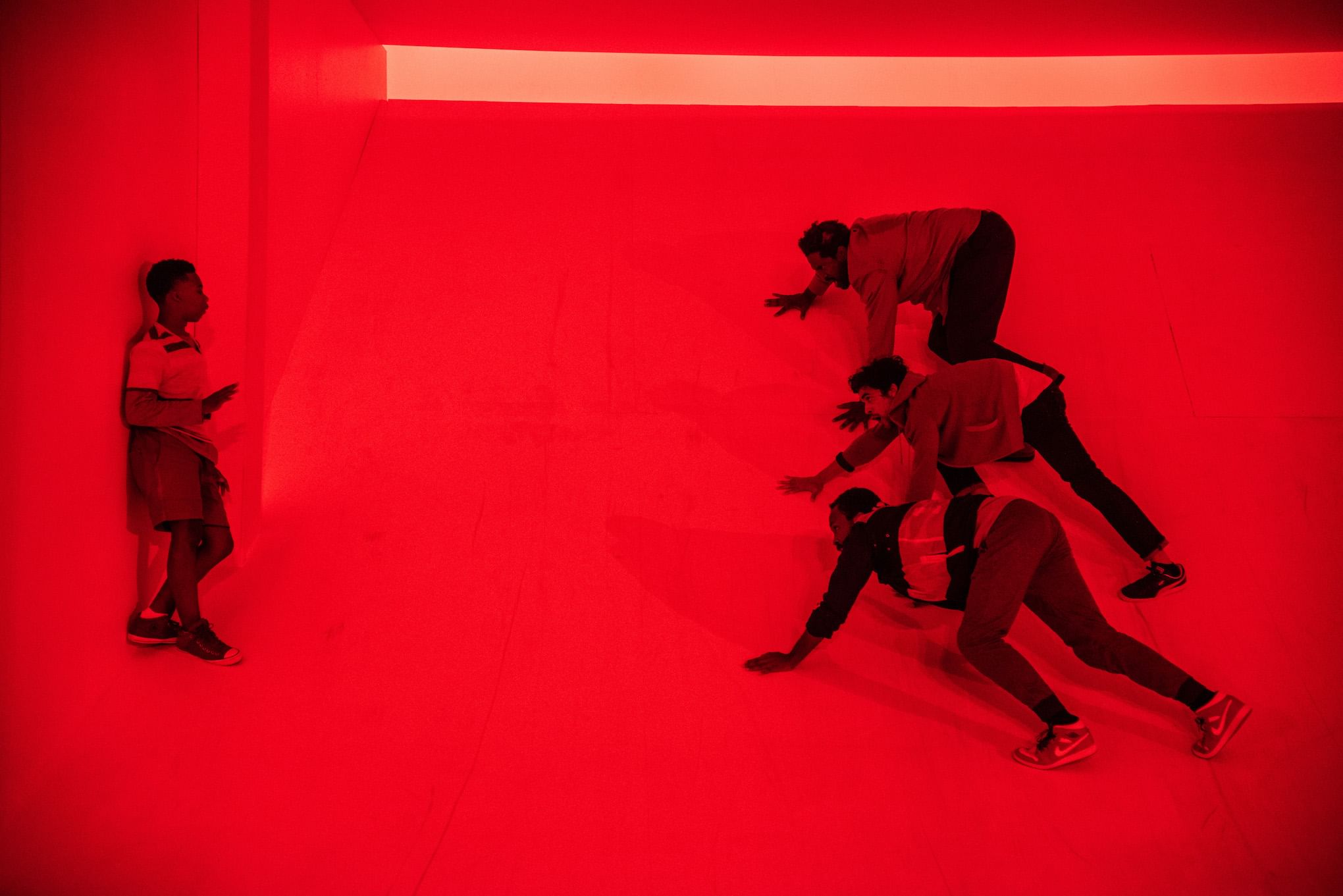 On a red-lit stage, four Black men crawl menacingly toward a Black boy.