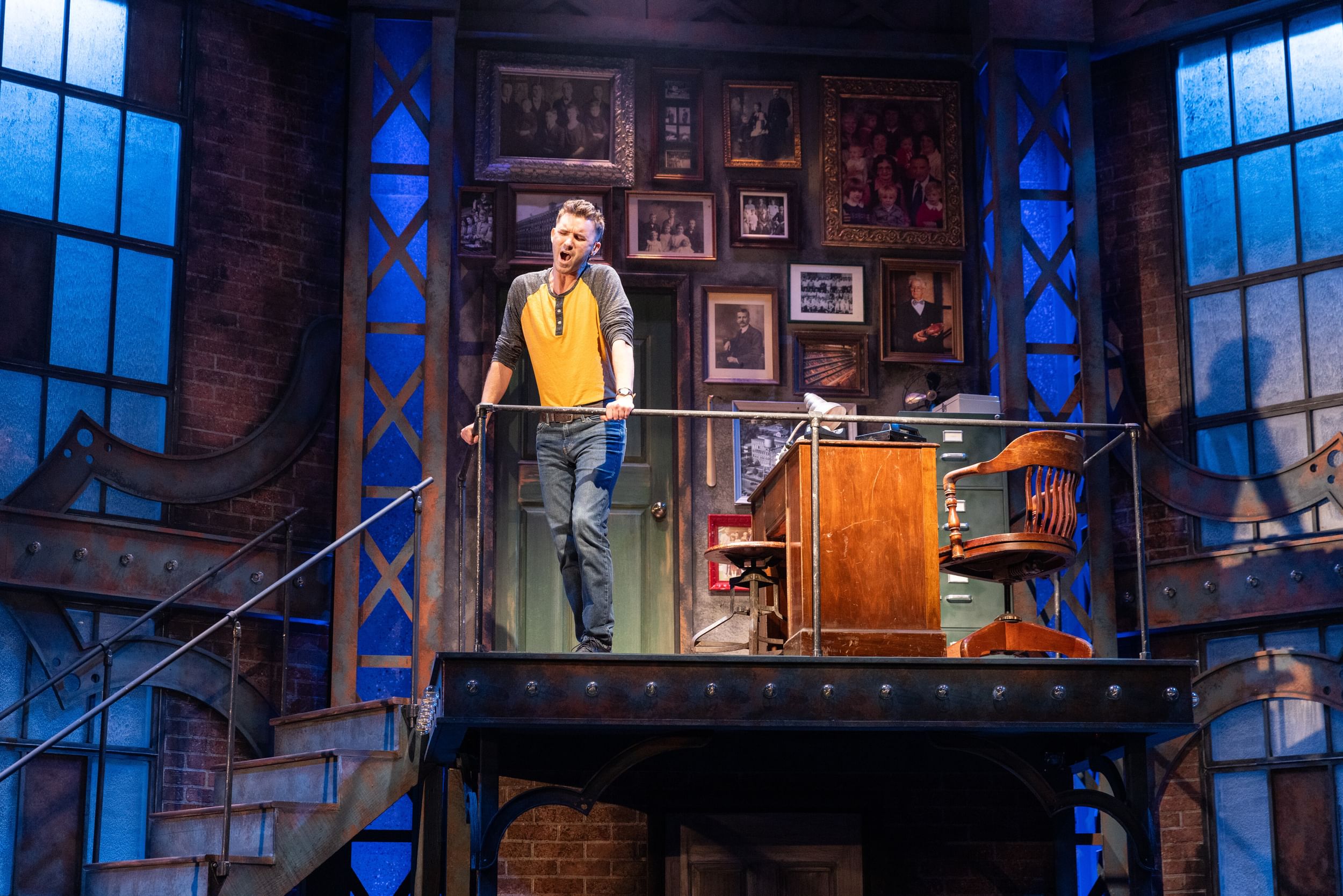 On a stage balcony decorated with vintage photos, Hoyak sings soulfully, wearing jeans and a yellow raglan tee.