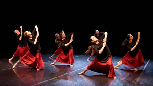 Women in loose black tops & flowing red skirts in the same pose: feet planted wide, hands together, one elbow pointed up