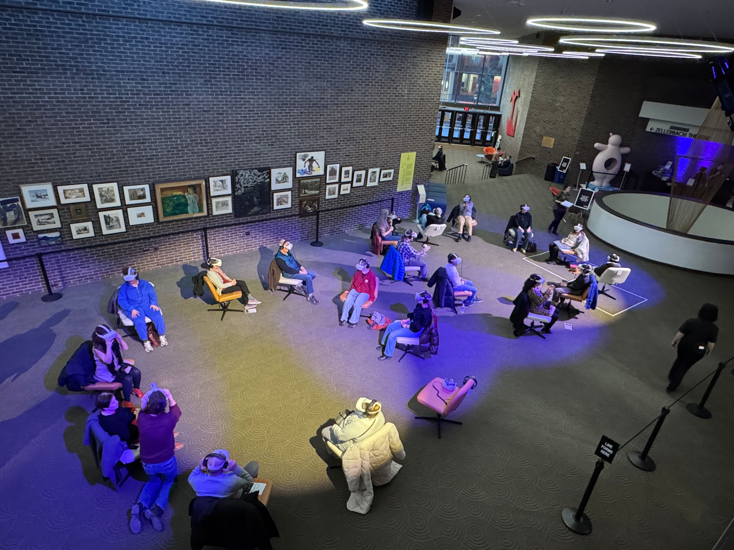 Photo taken from above shows two circles of people in swivel chairs and bulky VR headsets, facing different directions