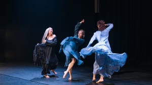 Three women spin joyfully in flowing long-sleeve dresses in shades of blue, seeming to float around them.