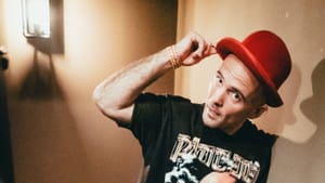 A portrait shot taken on indoor staircase, Kosha Dillz wearing a T-shirt with a performer’s face on it