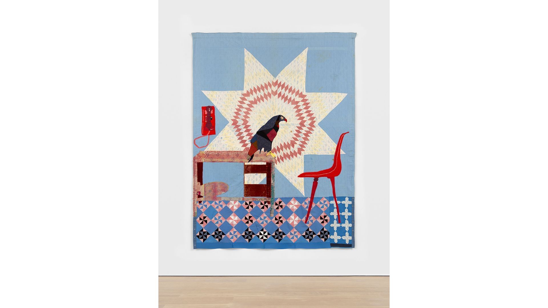 Quilt with a school (or prison?) desk, chair, and phone, with a large eagle on the desk, at the center of a patterned sun.