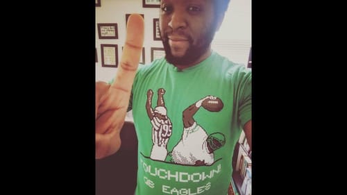 Kyle, a Black man, in a green shirt with vintage-looking pixel illustration of an Eagles referee & player spiking the ball