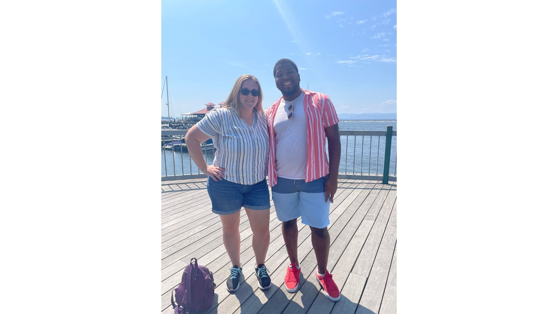 Alaina, in a blue striped top, poses smiling with Kyle, in a pink striped top, on a sunny dock by Lake Champlain.