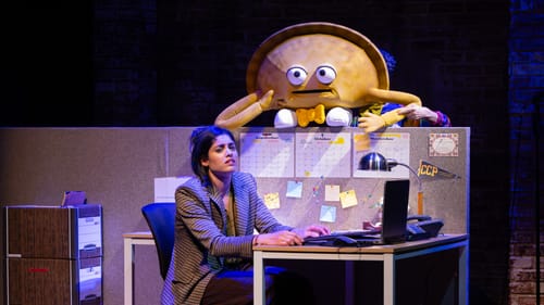 Rosa-Shapiro guides a puppet in the shape of a pastelito while González slumps exhausted in an office cubicle.