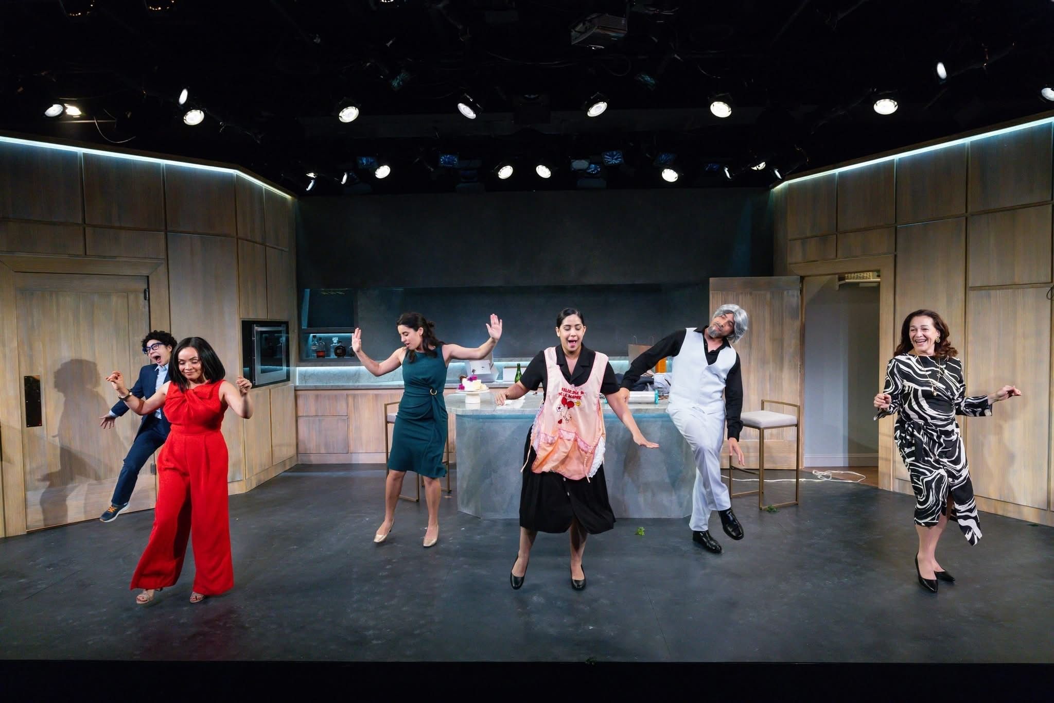 The six actors, most in semi-formal outfits, are all caught in different dance moves on a set that looks like a kitchen.