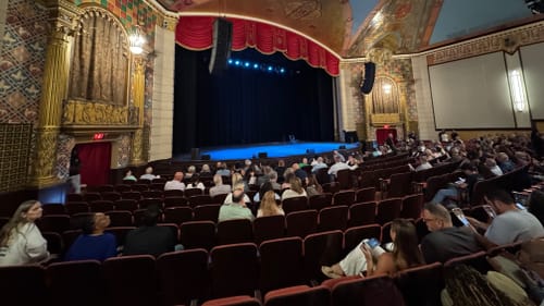 View from the seats inside the auditorium, with gold column accents and a high, ornately painted vaulted ceiling.