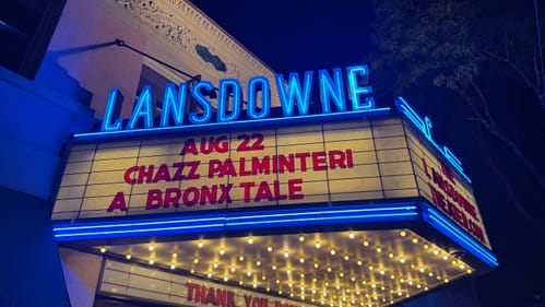 Close-up on the nighttime marquee, with neon blue letters, the show title in red letters, and little round lights underneath
