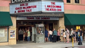 Daytime view of the theater’s 1920s-style marquee promoting the show, with a long line of people entering by the box office.