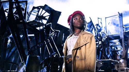 Against a misty, dramatic backdrop of the Les Mis barricade, a young Black woman in a red hat looks soulfully upward.