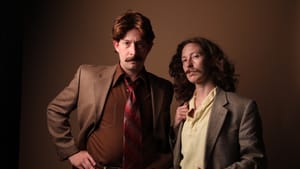 Looking serious in dour brown suits and mustaches, the actors pose together against a brown background.