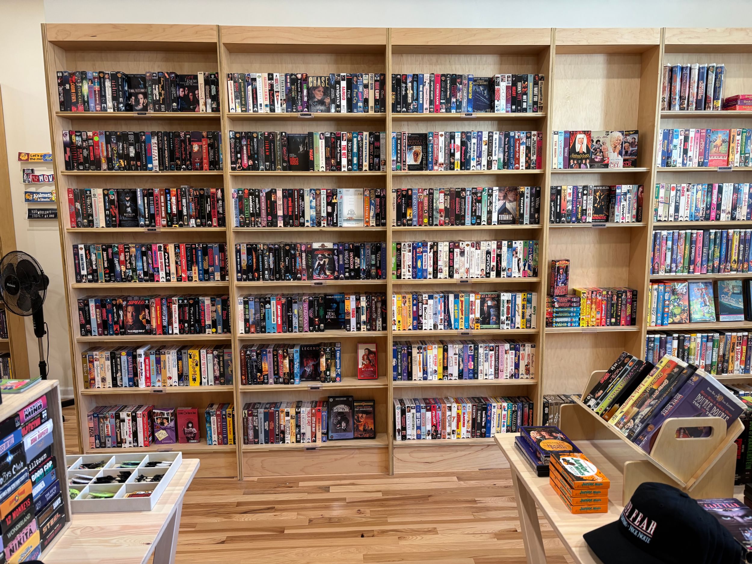 A selection of DVDs and VHS tapes are neatly organized on light wood shelves.