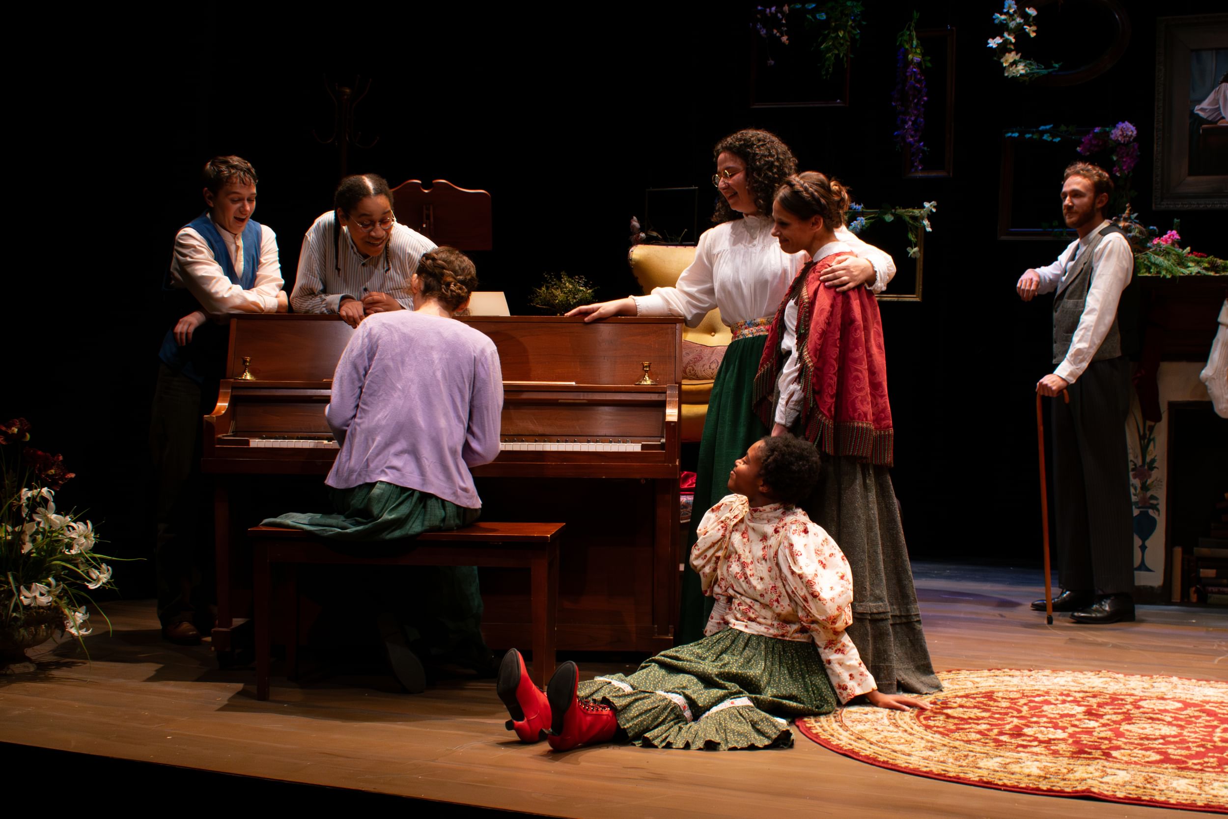 The multiracial ensemble, in 19th-century costumes, gathers lovingly around a piano onstage that one person plays.