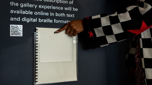 Close-up on a dark-skinned person reaching for the Braille text available in the ICA gallery.