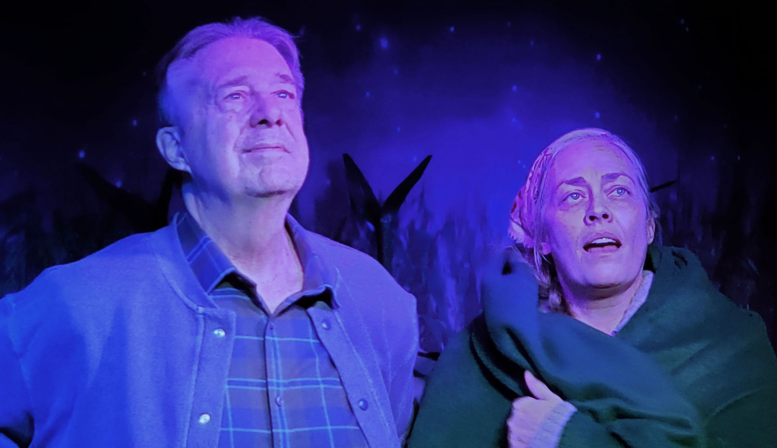 Bowersox and Moore, a white couple who appear to be in their 60s, look skyward in a wash of blue light.