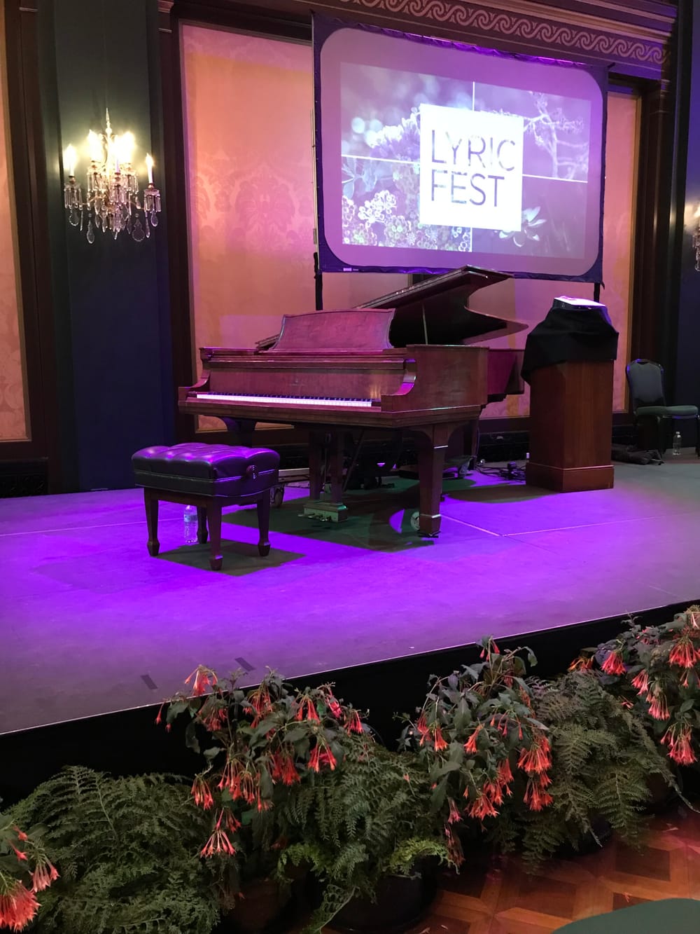 The Lyric Fest stage at Longwood Gardens, with a piano under purple lights. Fern-like plant with red flowers line the stage.