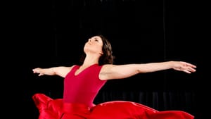 A dancer in a red dress that flows out wide, her arms stretched out long, on a stage with a black background