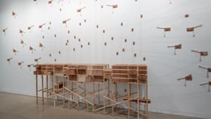 A delicate bureau-like wooden structure on long legs attaches to a complicated pulley and display system on the wall above.