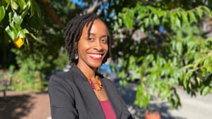 Anglin, a Black woman, poses in a black suit jacket, in an outdoor portrait.