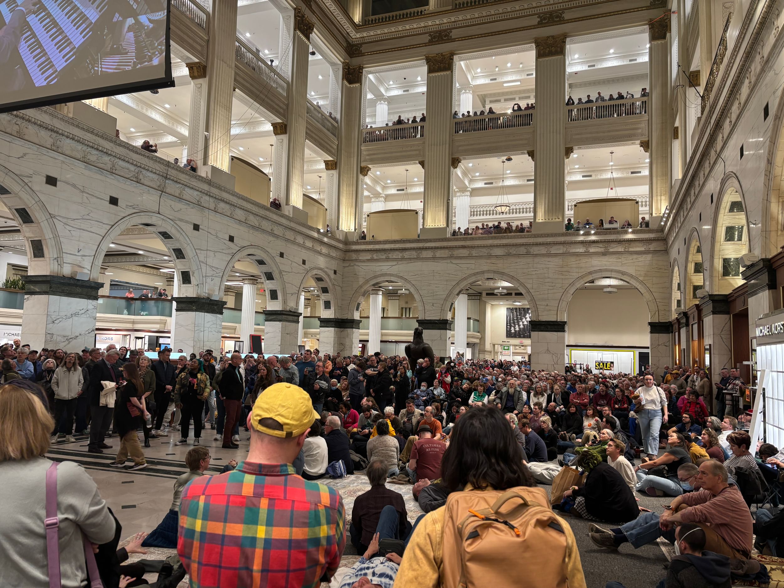 View from the ground floor of the grand multi-story hall of Macy’s, crowded with people listening to the organ.