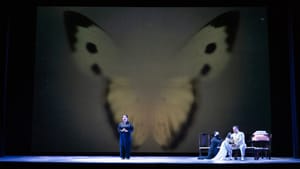 Small on stage, Ho, dressed in black, sings against a huge minimalist backdrop of butterfly wings, others onstage at right.