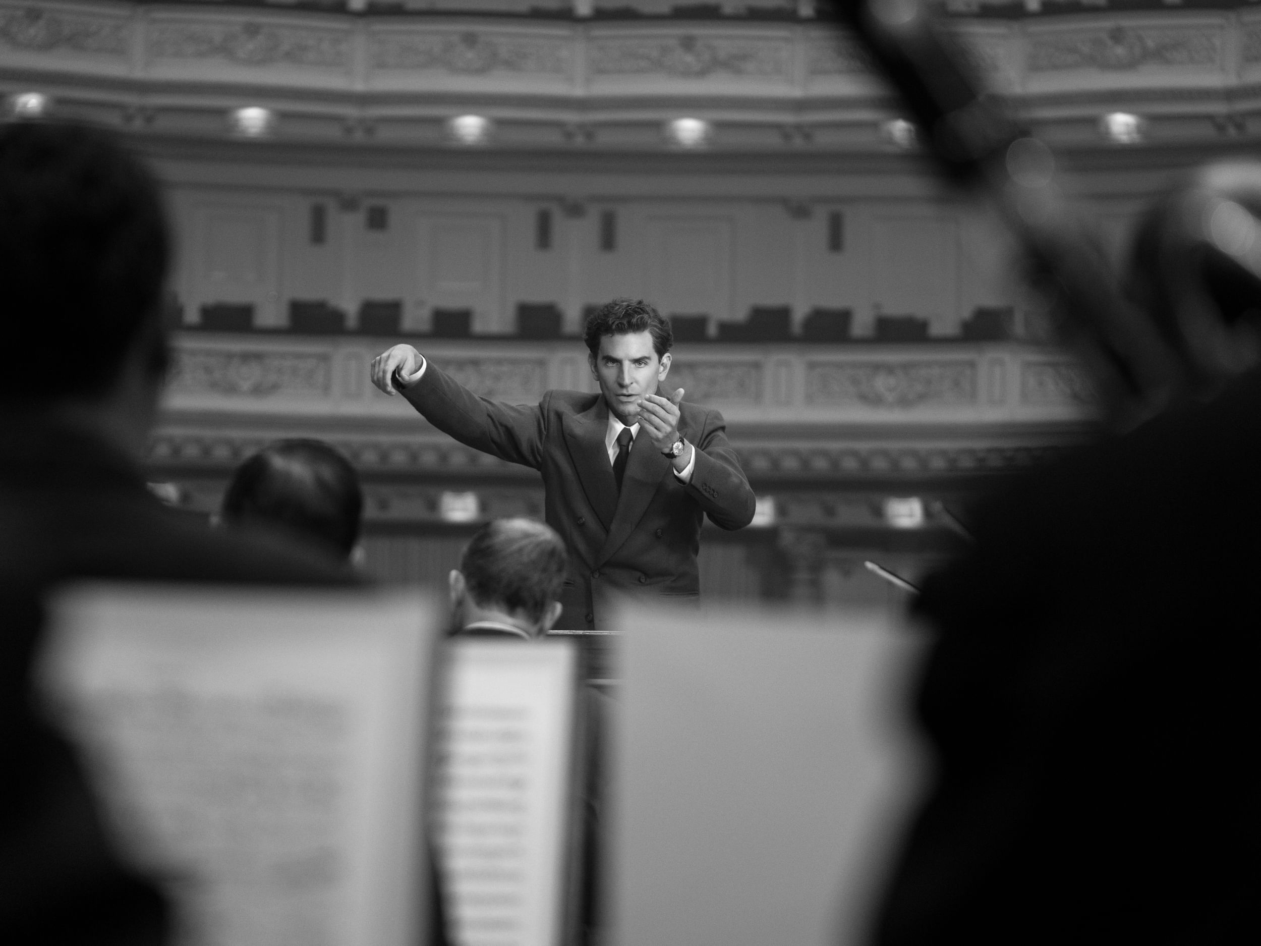 Black & white photo of Cooper as Bernstein conducting intensely, from the view of the musicians.