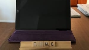 Wooden Scrabble tiles spell "Time to say goodbye" in front of the black screen of a sleeping tablet.