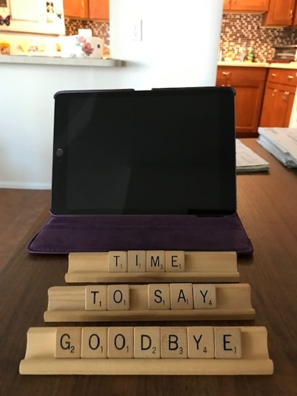 Wooden Scrabble tiles spell "Time to say goodbye" in front of the black screen of a sleeping tablet.