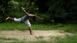 Hemmings in mid-movement over a sanded patch, grass and trees surround her