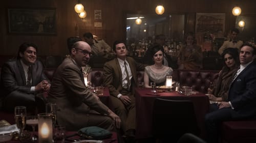 A scene from the movie. Six cast members sit in a dark, mirrored, wood-paneled bar, in a large leather booth.