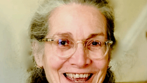Photo of Margaret, a white woman in her 60s with shoulder-length gray hair. She is smiling and wearing a red shirt.