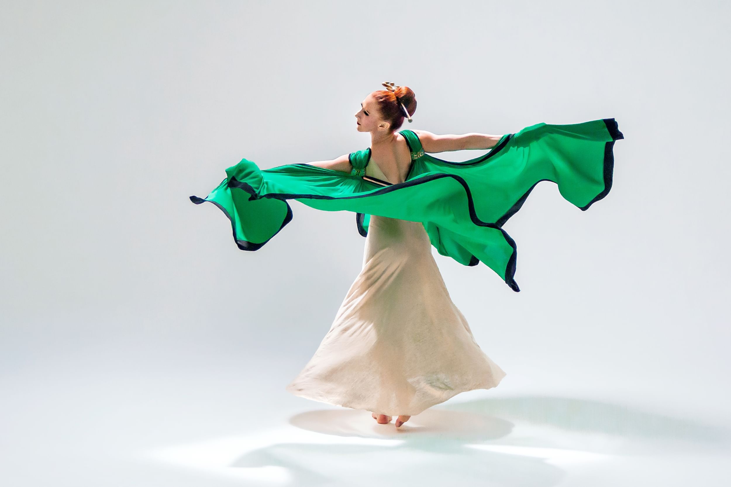 A dancer in a white dress and that has a green and black outer layer that flies in the air as the dancer moves