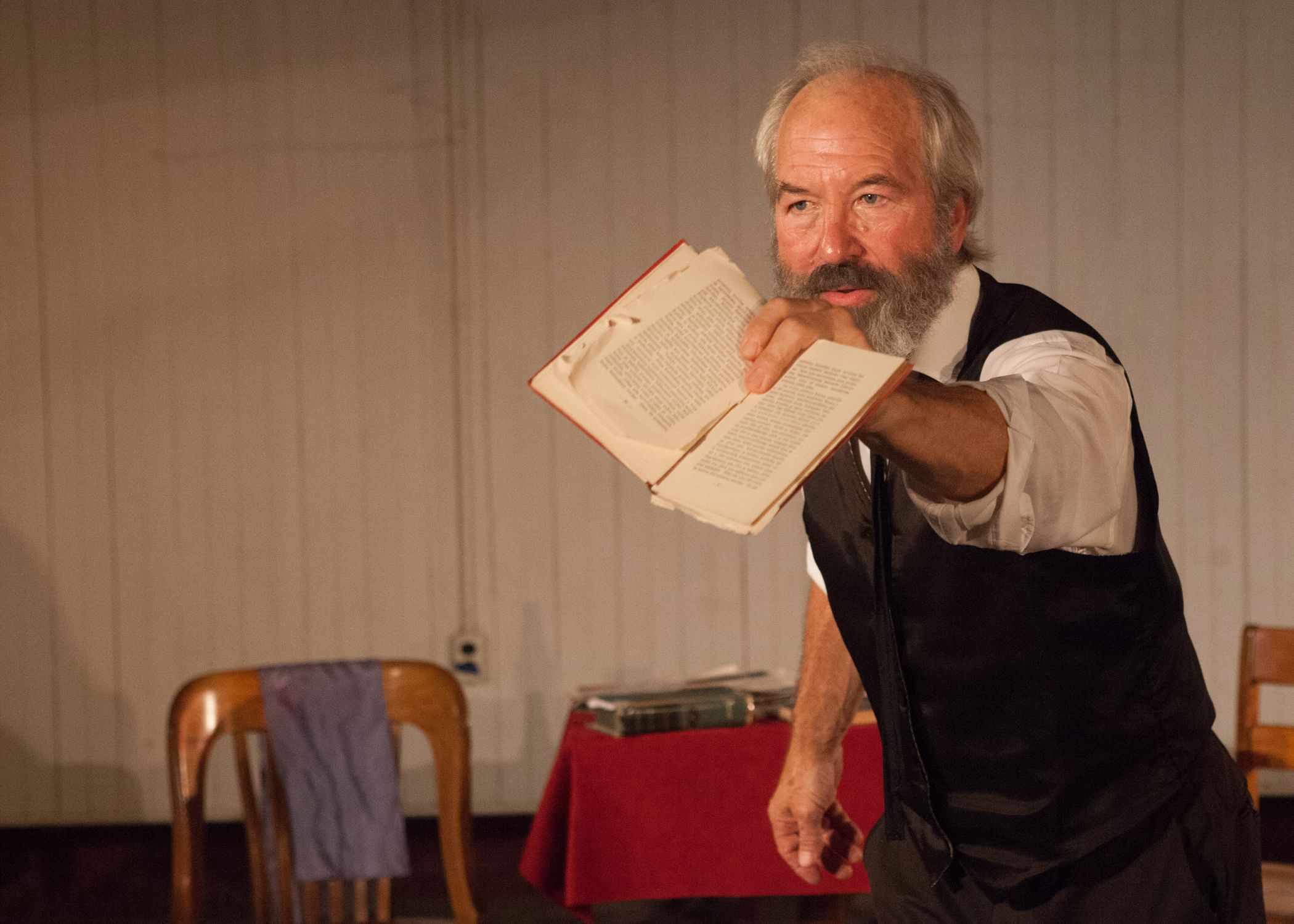 Weick, a white man with gray hair & beard, wearing a white shirt & black vest, urgently displays the pages of an old book
