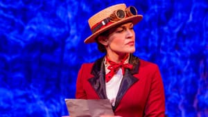 Gaffney as Poppins, wearing a red jacket with black lapels & a flat-brimmed straw hat with goggles on it. She holds a letter