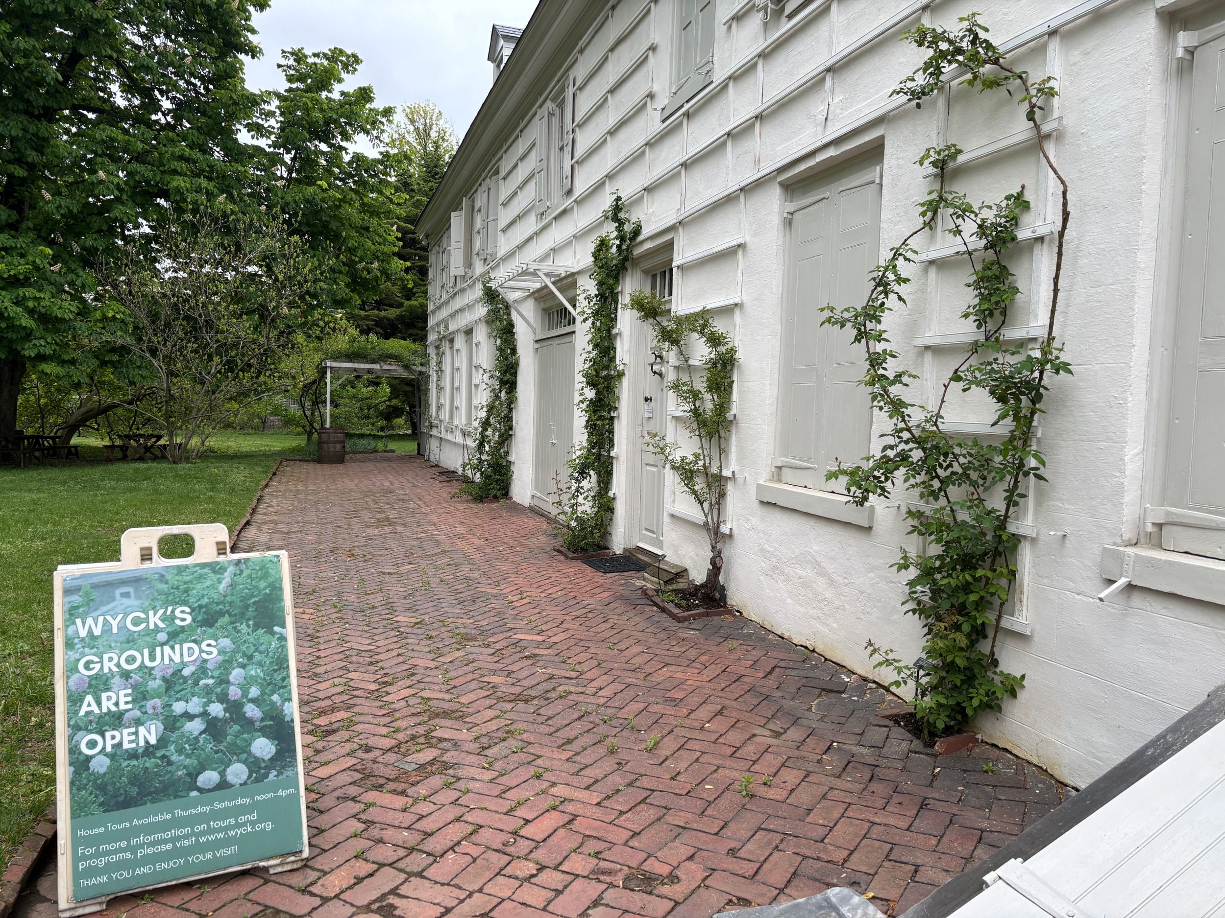 Outdoor view of a white-painted historic house with rose bushes growing up trellises and a red brick walkway.