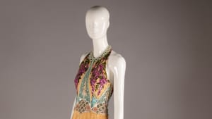 A gold, slender halter-style dress with a long, delicate pleated skirt and opulent beaded bodice in muted purple and blue.