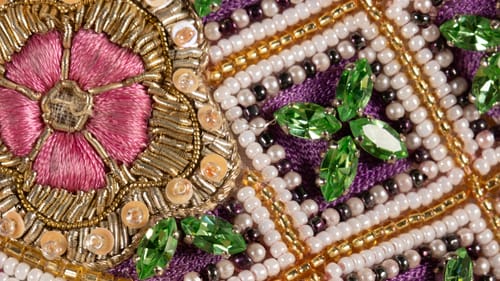 Close-up on complex, opulent design with jewels, beads & embroidery in green, purple, gold, pink, black, and pearl.