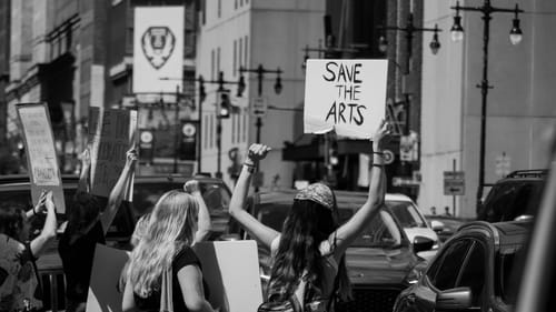 Black & white photo of students protesting on Broad Street, seen from behind with their arms raised, carrying signs