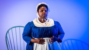 Tiffany Bacon performs as Freeman, a Black woman. In blue and white frock and slip of coarse.