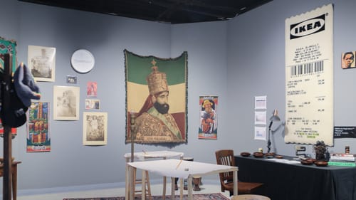 Photo of the studio, with pattered rug, vintage multicultural portraits, and a realistic weaving like an IKEA receipt