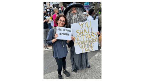 Strong holds a sign saying “a better world is possible” while Gandalf’s says "You shall not pass discriminatory voting laws"