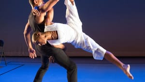 Rainey with another dance partner in mid move, holding them up in a rehearsal space.