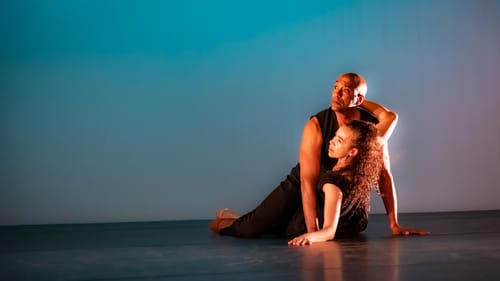 Rainey, a Black man, looks to the left with his body angled off the ground, Moss-Thorne beneath with one arm around his neck.