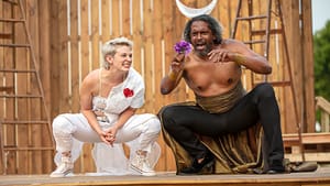 Actors Mary Tuomanen, wearing white, and Lindsay Smiling, wearing black, crouch and plot gleefully over a purple flower