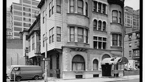 Black & white photo of a gracious five-story city building with a stone front, arches and bay windows.